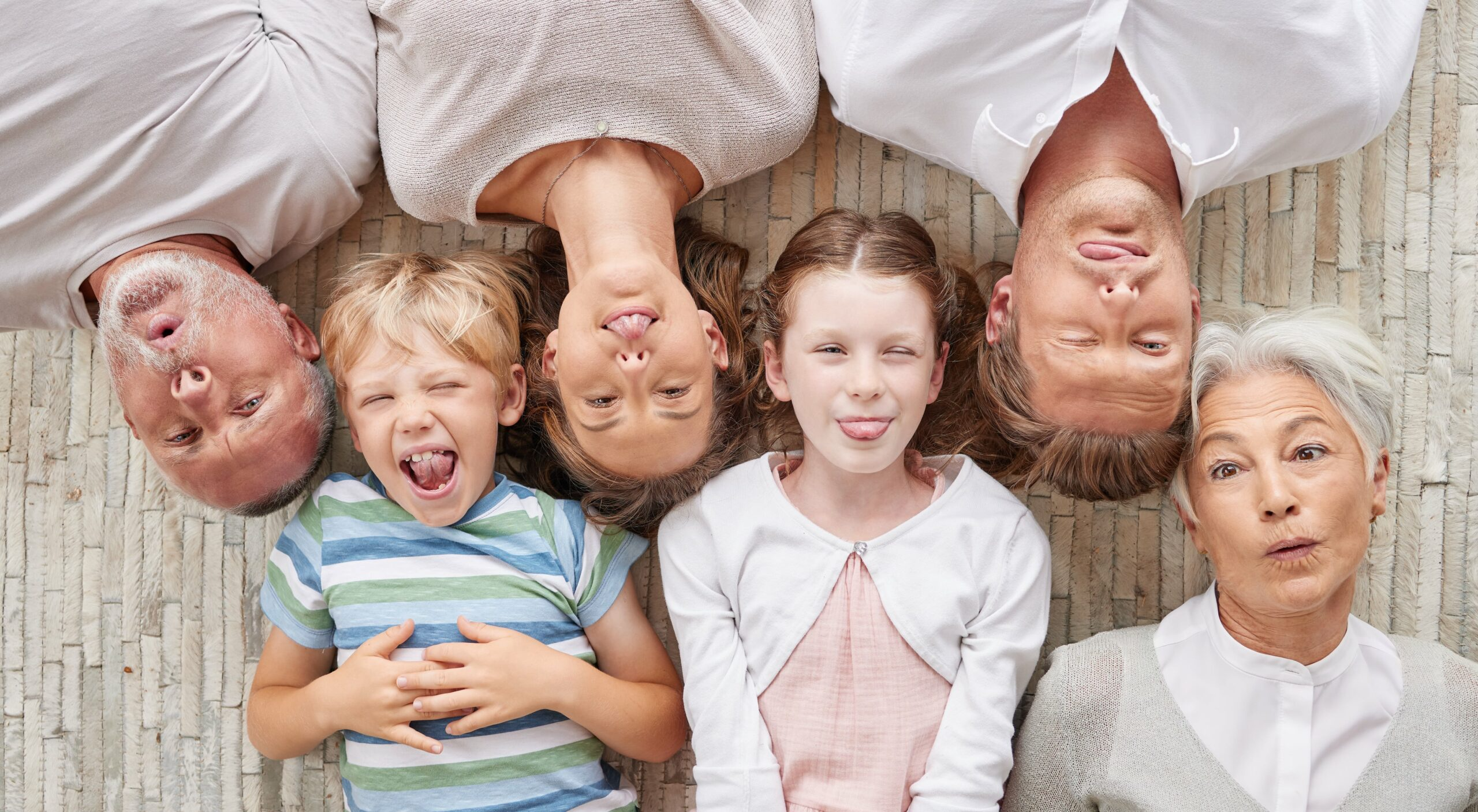 family bonding together being playful showing different expressions while bonding enjoying quality time happy fun family making silly faces lying together living floor home min scaled