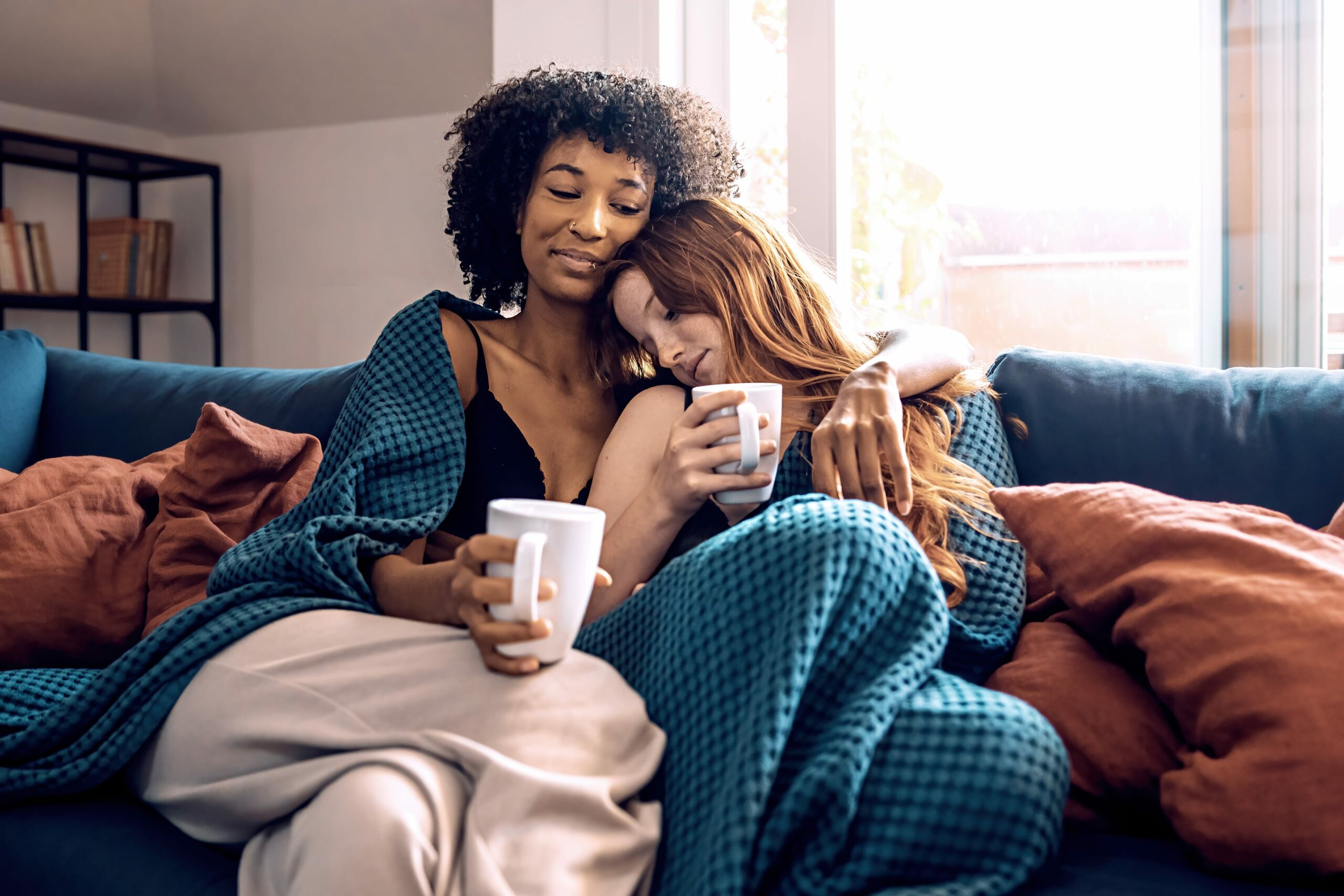 multiethnic lesbian couple hugging drinking coffee sofa home lgbt lifestyle concept min scaled